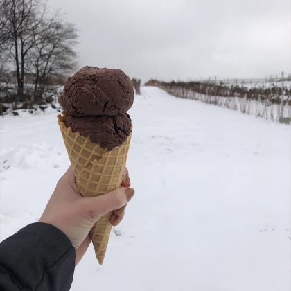 Person holding a waffle cone of chocolate ice cream with a snowy background