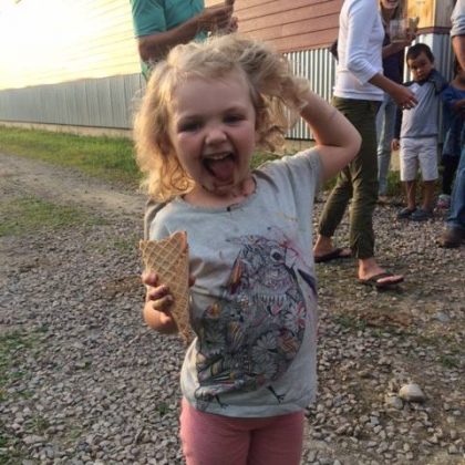 Young girl with curly blonde hair holds an ice cream cone and has chocolate ice cream dripping down her chin