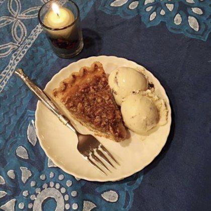 a holiday desert on a blue tablecloth: pecan pie with white ice cream and a tea candle